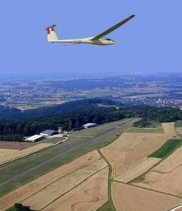 Segelflug über einem Feld mit Bäumen und Gebäuden im Hintergrund, mit Text am oberen Bildrand.