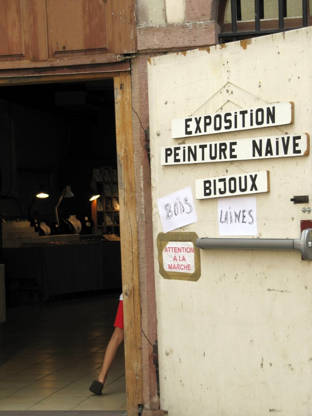 Ein Innenblick in eine Unterkunft mit einer Person im Hintergrund neben Treppe und Lampen sowie einer Tür auf der rechten Seite mit Brettern und Text.