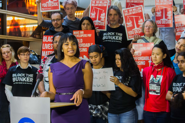 Eine Black Lives Matter-Aktivistin spricht an einem Podium mit Mikrofon zu einer Menge mit Schildern.