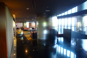Eine geräumige Business-Lounge am Hong Kong International Airport mit großen Fenstern, hohen Decken mit elektrischem Licht, Sitzgelegenheiten wie Stühle und Sofas, Tischen, einem Teppichboden und einer zentralen Säule.
