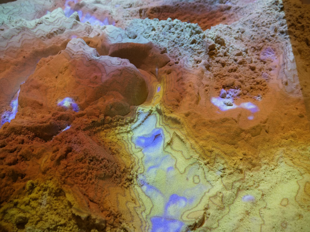 Nahaufnahme einer detaillierten 3D-Karte einer Wüstenlandschaft, die sandfarbene Berge, Täler und Kämme unter heller Beleuchtung zeigt.