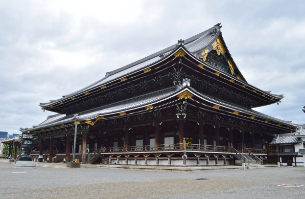 Ein großes Gebäude mit zahlreichen Fenstern, der Nara-Schrein, umgeben von verschiedenen Strukturen und Grünflächen, mit einer Straße im Vordergrund und dem Himmel im Hintergrund.