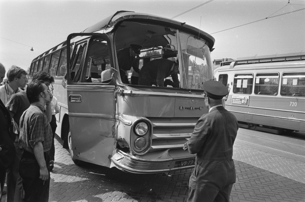 Schwarz-weißes Bild einer Gruppe von Menschen, die um einen verunglückten Bus auf der Straße stehen, mit anderen Fahrzeugen im Hintergrund.