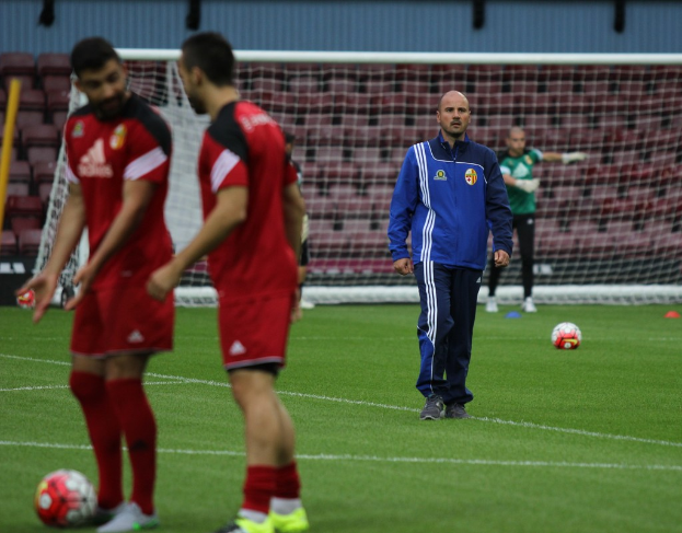 Ein Fußballfeld mit darauf stehenden Spielern, zwei Bälle sind sichtbar und im Hintergrund ist das Stadion leer.