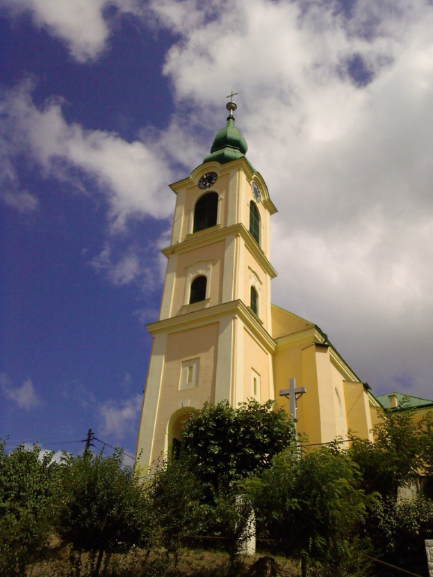Eine Kirche mit Kreuzen in der Mitte, umgeben von Bäumen, einem Pfahl und Drähten unten und dem Himmel oben.