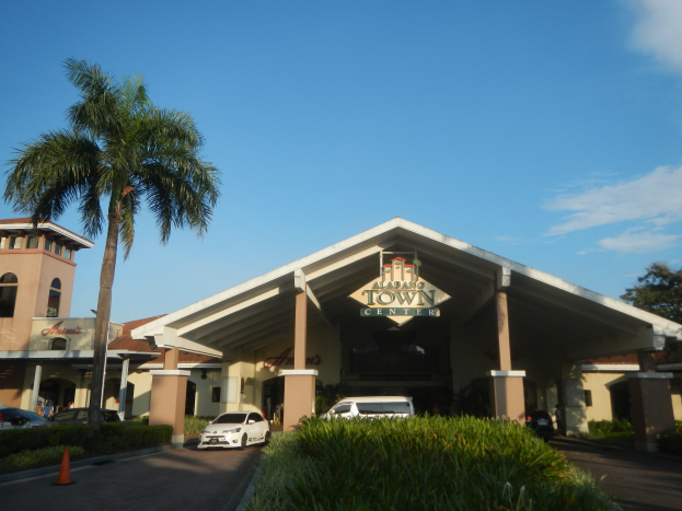 Der Eingang eines Resorts mit Palmen vorne, umgeben von Gebäuden, Kraftfahrzeugen auf der Straße, Verkehrskegeln, Büschen, Bäumen und einem bewölkten Himmel im Hintergrund.