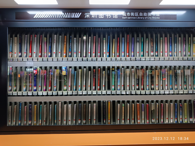 Eine gut beleuchtete Bibliothek mit zahlreichen Büchern auf Regalen, ein Textschild und ein Wasserzeichen unten, das an eine Selbstbedienungsbibliothek von Stadtvierteln erinnert.