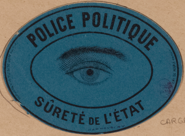 Ein brauner Karton mit einem blauen Aufkleber, der "Polizei Politique Surete de L'Etat" und ein Auge in der Mitte trägt.