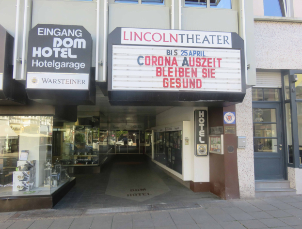 Außenansicht des Lincoln Theaters in Berlin, Deutschland, mit Glasfenstern und -türen sowie einer Schautafel und einem Innenblick, der ein städtisches Durcheinander von Gegenständen zeigt.