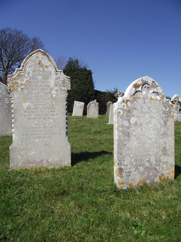 Ein Friedhof mit zahlreichen Gräbern, grünem Rasen und Bäumen mit Himmel im Hintergrund.