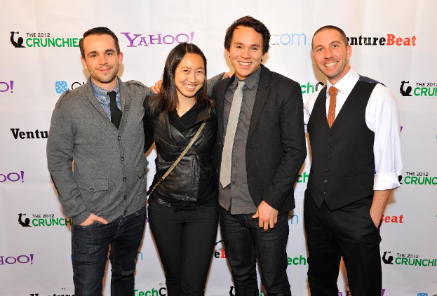 Eine Gruppe von lachenden Menschen, die vor einer Sponsorenflagge posieren.