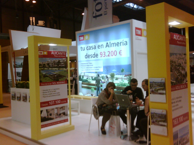 Eine Gruppe von Menschen, die um einen Tisch herum auf Stühlen sitzen und auf einen Laptop schauen und arbeiten, mit mehreren Flyern mit verschiedenen Anzeigen daneben.