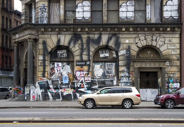 Gebäude mit Graffiti, Gittern, Treppen, Geländern, Himmel und Fahrzeugen auf der Straße.