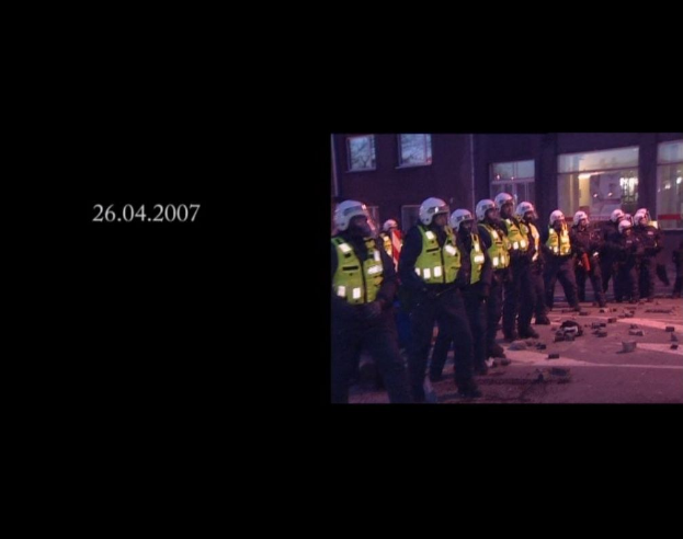 Eine Gruppe von Polizisten in Helmen und Jacken steht vor einem Gebäude mit Fenstern, mit einem Datum auf der linken Seite.