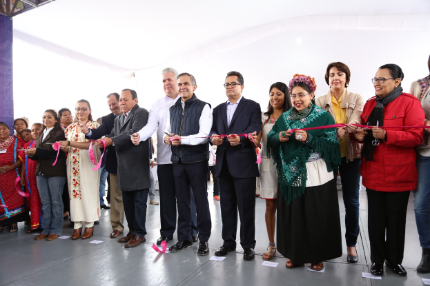 Eine Gruppe von Menschen bei einer Scherenschnitte-Zeremonie, die strahlend eine Schere halten, mit Papieren auf dem Boden und einem weißen Tuch im Hintergrund.