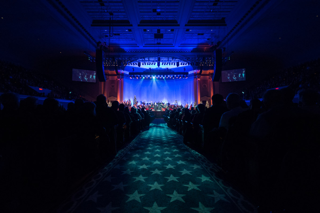 Ein großer Auditorium mit Sitzenden, eine Bühne mit Musikern und eine Decke mit Lichtern und Fernsehern, was auf einen Konzertsaal für die nationale Konferenz 2019 hindeutet.