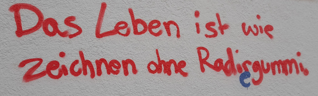 Eine weiße Wand mit kräftigem rotem und blauem Graffiti, das "Das Leben ist wie zeichnen dhe Radisgumm" lautet.