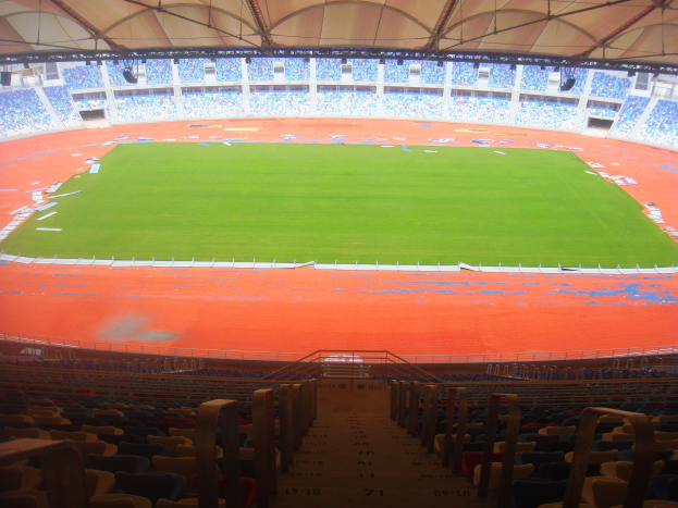 Großes Stadion mit vielen Zuschauern, Sitzreihen, Geländern, Treppen und Dach, mit dem Spielfeld in der Mitte sichtbar.