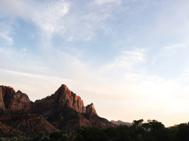 Ein atemberaubender Blick auf den Zion-Nationalpark in Utah, der Bäume, Hügel und einen von der untergehenden Sonne erleuchteten Himmel zeigt.
