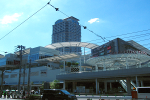 Eine belebte Stadtstraße mit Fahrzeugen, Fußgängern, Strommasten, Bäumen, Gebäuden und einem hohen Gebäude.