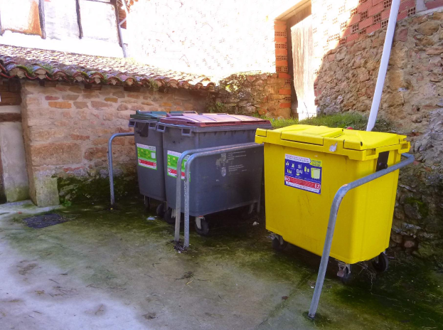 Zwei gelbe und graue Mülltonnen mit Rollen stehen nebeneinander vor einem Gebäude mit einer Wand und einem Fenster im Hintergrund.
