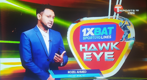 Ein Mann in einem blauen Anzug steht vor einem Fernseher mit einem Logo und Text und trägt ein Mikrofon, was darauf hinweist, dass er ein Cricket-Analyst ist.