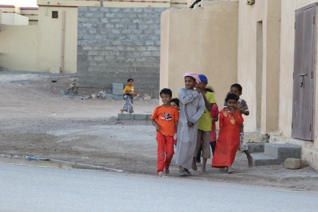 Eine Gruppe strahlender Kinder vor Gebäuden, Wasser, Felsen und einer Straße.
