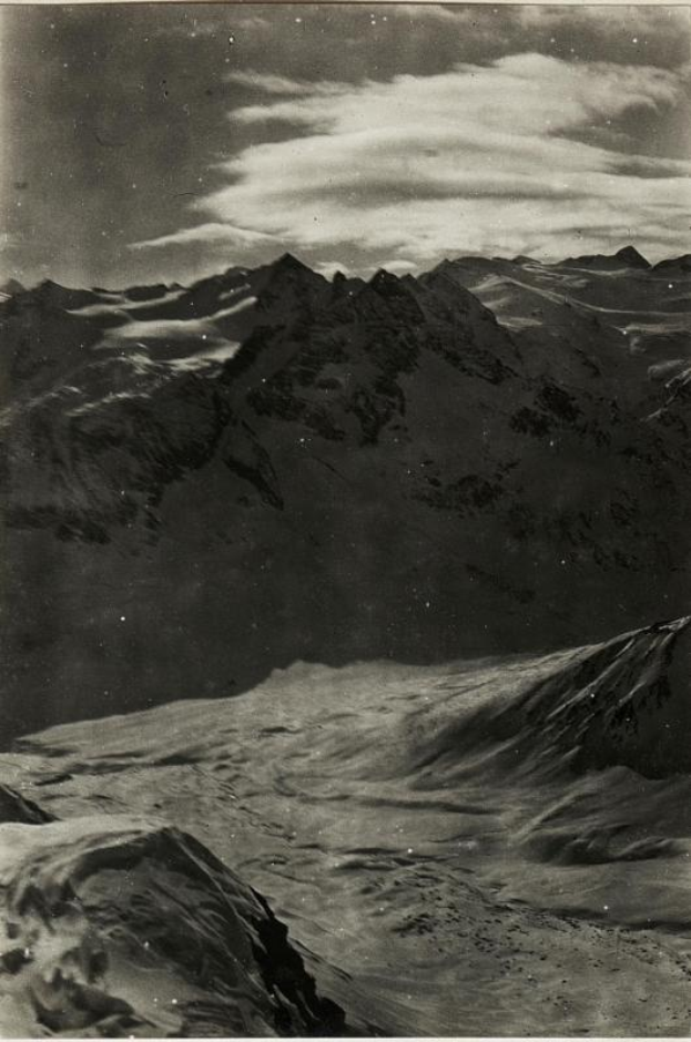 Ein Schwarz-Weiß-Foto einer schneebedeckten Gebirgskette mit einem bewölkten Himmel und einem Text unten, der 'Gustav Klimt - Die Alpen' lautet.