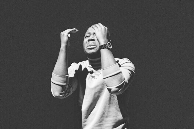 Ein Mann steht mit den Händen auf dem Kopf vor einem schwarzen Hintergrund, trägt ein T-Shirt und eine Uhr und sieht besorgt aus, wahrscheinlich wegen einer Festnahme im Zusammenhang mit einem Raub.