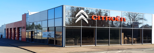 Außenansicht einer Citroen-Vertretung mit Glaswänden und -türen, einer Straße davor und einem klaren blauen Himmel.