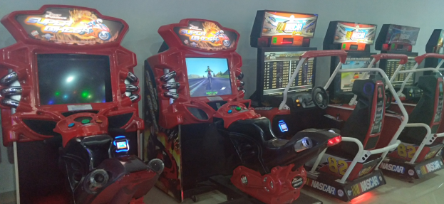 Eine Reihe buntfarbiger Arcade-Rennwagen-Maschinen auf einem gefliesten Boden mit einer Wand im Hintergrund.