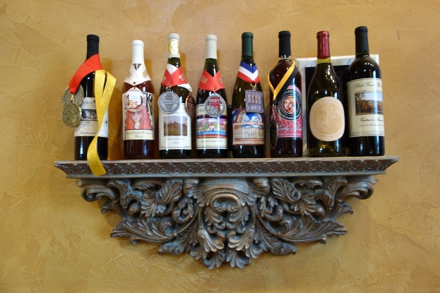 Mehrere Weinflaschen auf einem Regal, eine mit einem sichtbaren Medaillon, vor einer hellgelben Wand.