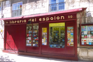 Ein rotes Schirmchen-Buchgeschäft namens "Libreria del Espolon" mit ordentlich sortierten Büchern drinnen, das sich in einem Gebäude mit Fenstern und Geländern befindet.