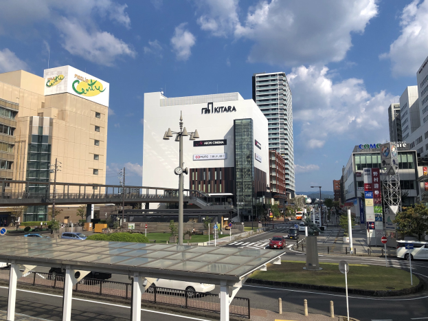 Eine belebte Stadtstraße mit Fahrzeugen, hohen Gebäuden, Straßeninfrastruktur, Grünfläche, einer Brücke und einem bewölkten Himmel.