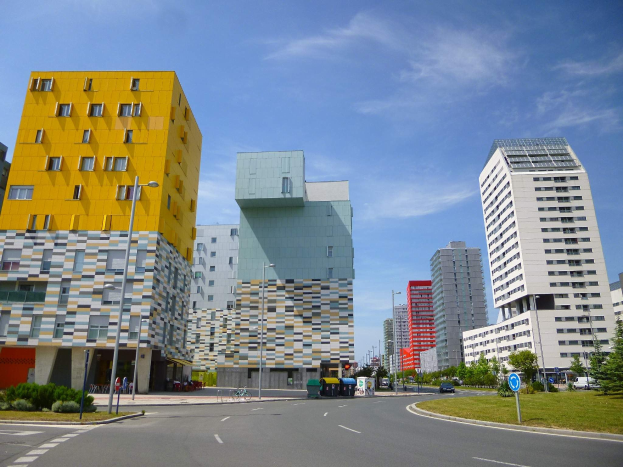 Eine Stadtstra├če mit hohen Geb├Ąuden, die als Teil der Universit├Ąt Rotterdam bezeichnet sind, Laternenpf├Ąhle, Stra├čenlaternen, Kraftfahrzeuge, Informations├Ąnder, Str├Ąucher, B├Ąume und ein bew├Âlktes Himmel.