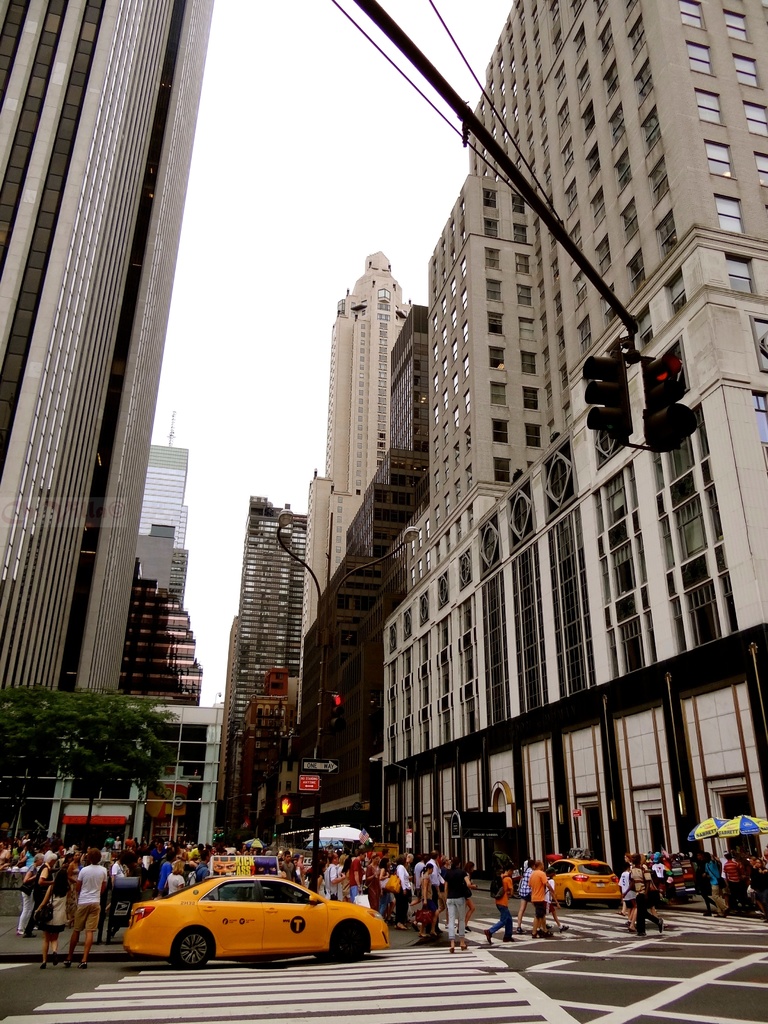 Eine Stadtansicht mit Gebäuden, Ampeln, Fenstern, einigen Fußgängern, Autos und Himmel.