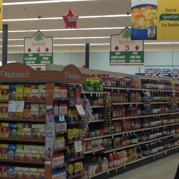 Ein Supermarktinneres mit Regalen voller Lebensmittel, Deckenleuchten und Schildern.