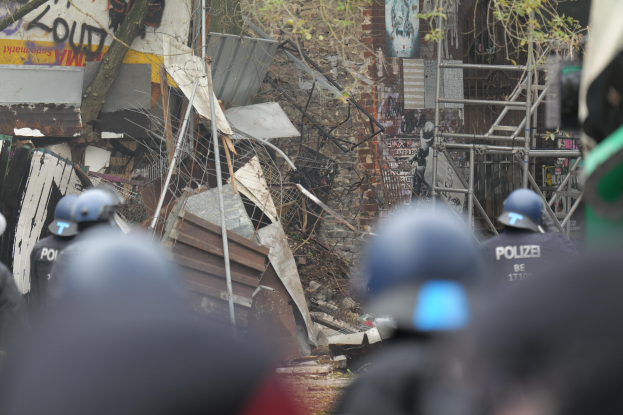 Gruppe von Polizisten in Helmen vor einem demolierten Gebäude, umgeben von Bäumen, Masten und Trömmern.