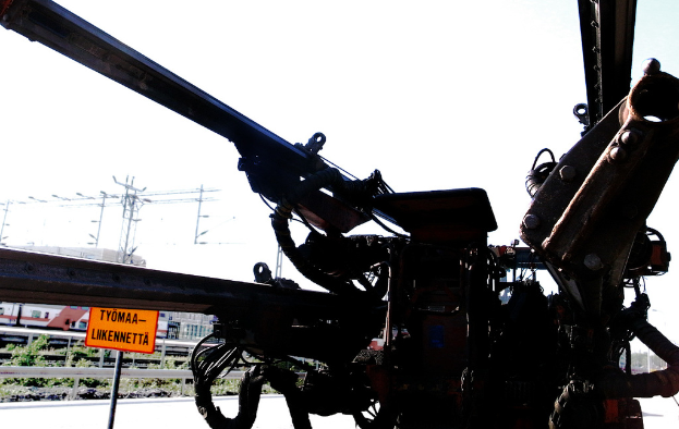 Eine Maschine ist im Vordergrund mit elektrischen Masten, Kabeln, Absperrungen, Pflanzen und Himmel im Hintergrund.