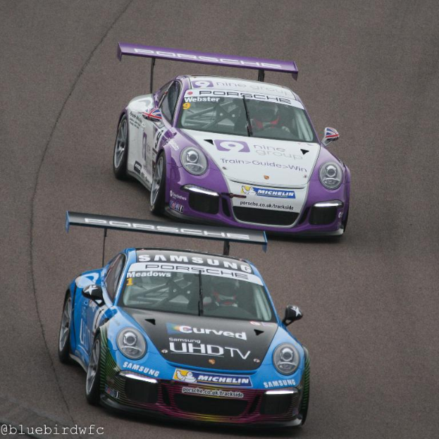 Zwei Autos fahren auf einer Straße außerhalb einer Stadt mit Text in der linken unteren Ecke.