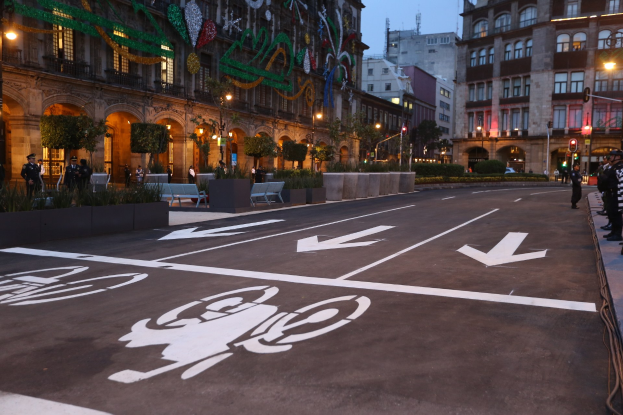 Eine Stadtstraße mit einem ausgewiesenen Fahrradweg, gesäumt von Gebäuden, Straßenmöbeln und Grünflächen unter einem klaren blauen Himmel.