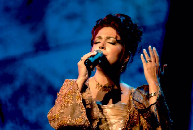 Frau in goldnem Kleid, die auf der Bühne der Eurovision Song Contest in ein Mikrofon singt, mit blauem und schwarzem Hintergrund.