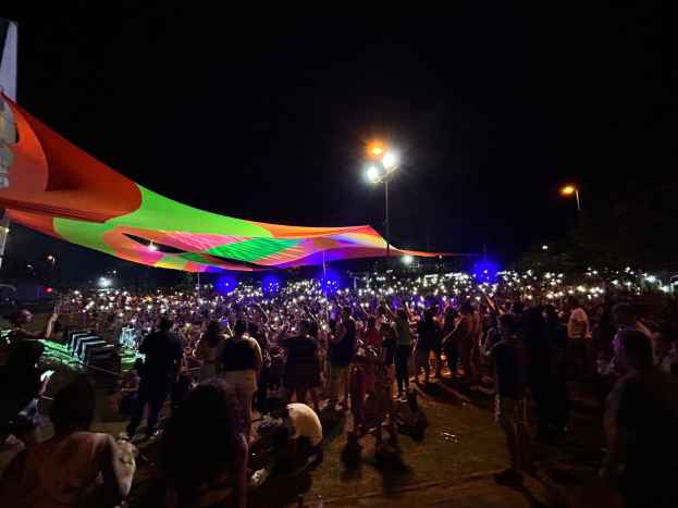 Eine große Menschenmenge steht vor einem hell erleuchteten Zelt bei Nacht während des Festivals der Künste 2018, mit bunten Lichtern, beleuchteten Pfählen, einem Gebäude auf der linken Seite und dem Nachthimmel im Hintergrund.