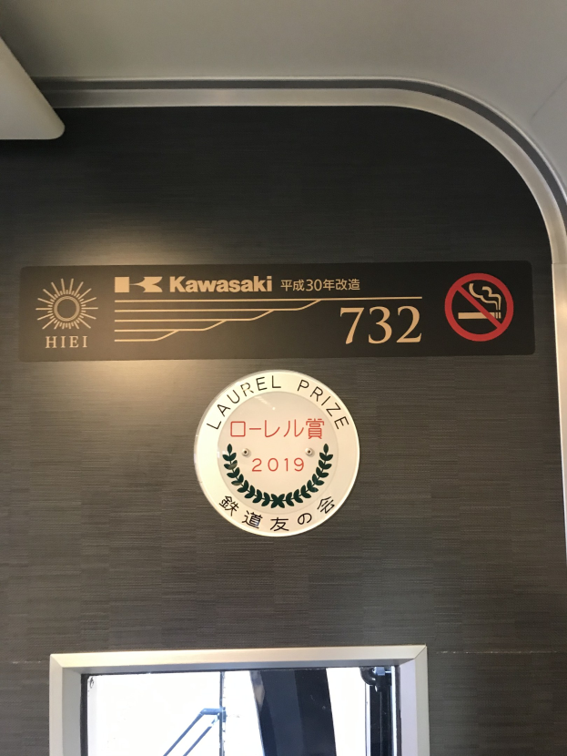 Wand mit einem Schild, auf dem "Kawasaki 732" steht, und einem Glasfenster rechts daneben.