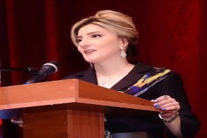 Eine Frau steht an einem Podium mit einem Mikrofon, spricht vor einem roten Vorhang, wahrscheinlich über Frauenrechte.