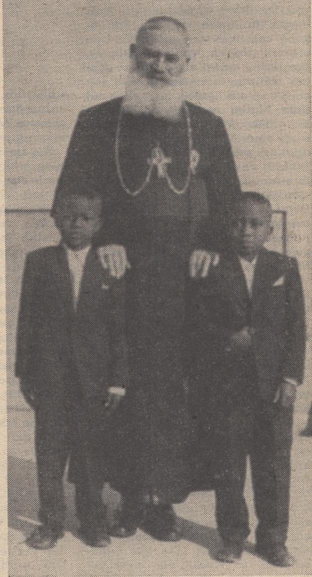 Ein Schwarz-Weiß-Foto eines Mannes, der neben zwei Jungen in Blazern und Krawatten steht, mit einem Text unten, der darauf hinweist, dass er ihr Vater ist.