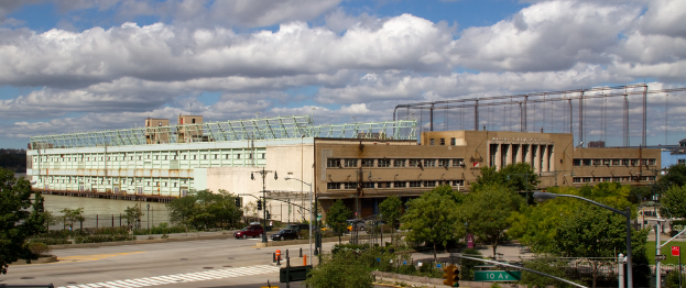 Eine Straße mit Fahrzeugen, Bäumen und Straßenlaternen, die zu einem großen Gebäude in der Nähe einer Wasserfläche führt.