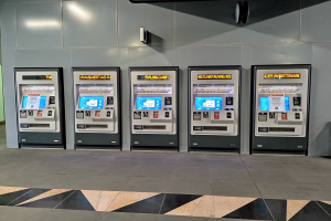 Eine Reihe von Automaten für den Verkauf von Eintrittskarten auf einem gefliesten Boden mit einer Wand und Deckenleuchten im Hintergrund.