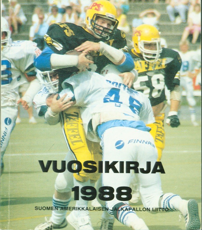 Gruppe von Menschen in Sportbekleidung und Helmen, die Fußball auf einem Feld spielen, mit Zuschauern auf einer Treppe im Hintergrund; Text unten lautet "Vuosikirja 1988 - Suomen Amerikkaisen Jalkapallon Litto".