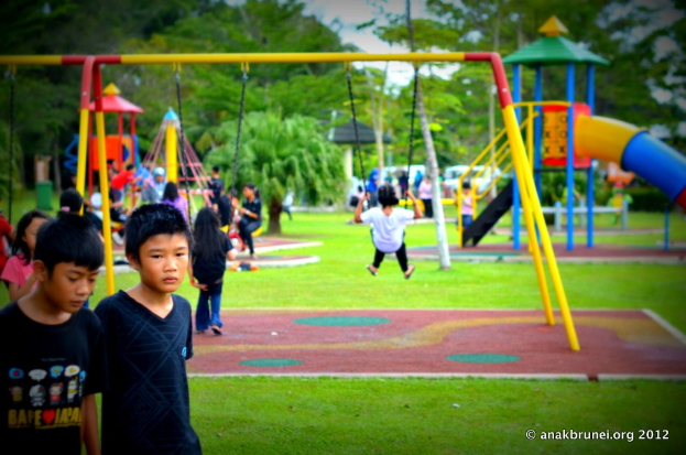 Kinder spielen in einem Park mit Spielgeräten und Bäumen.
